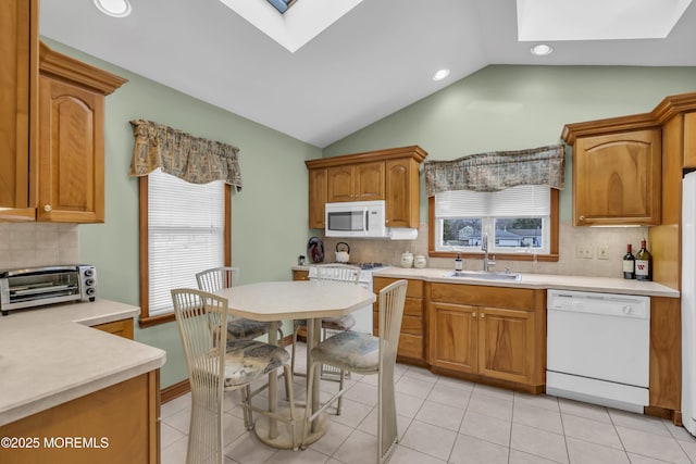 kitchen with vaulted ceiling with skylight, white appliances, sink, backsplash, and light tile patterned flooring