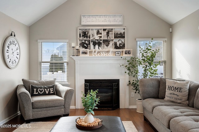 living room featuring wood-type flooring, a tiled fireplace, plenty of natural light, and lofted ceiling