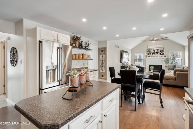 kitchen with light hardwood / wood-style floors, white cabinetry, high end fridge, a kitchen island, and lofted ceiling