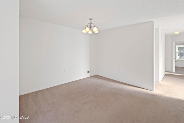 carpeted spare room with a textured ceiling and a chandelier