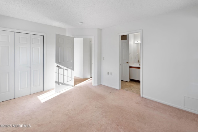 unfurnished bedroom featuring ensuite bath, light carpet, a closet, and a textured ceiling