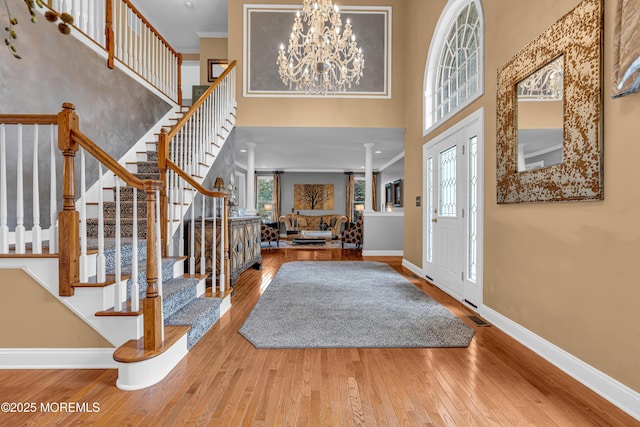 foyer entrance with a high ceiling, wood-type flooring, an inviting chandelier, ornamental molding, and decorative columns