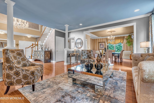 living room with crown molding, light wood-type flooring, an inviting chandelier, and ornate columns