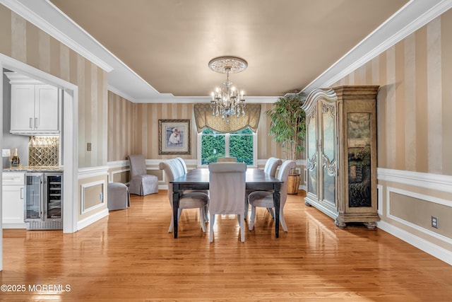 dining room featuring beverage cooler, ornamental molding, bar, a chandelier, and light hardwood / wood-style flooring