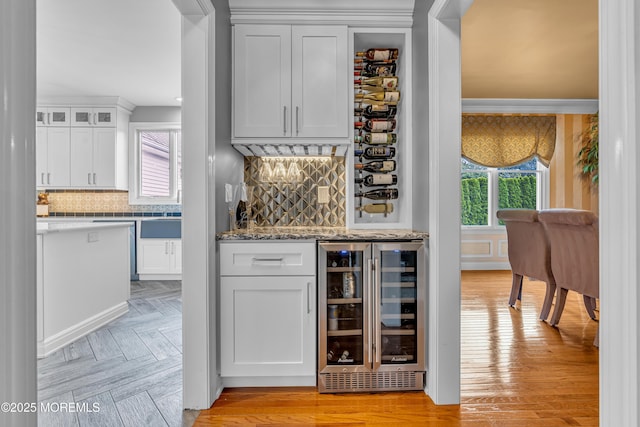 bar with backsplash, white cabinetry, light stone countertops, and beverage cooler