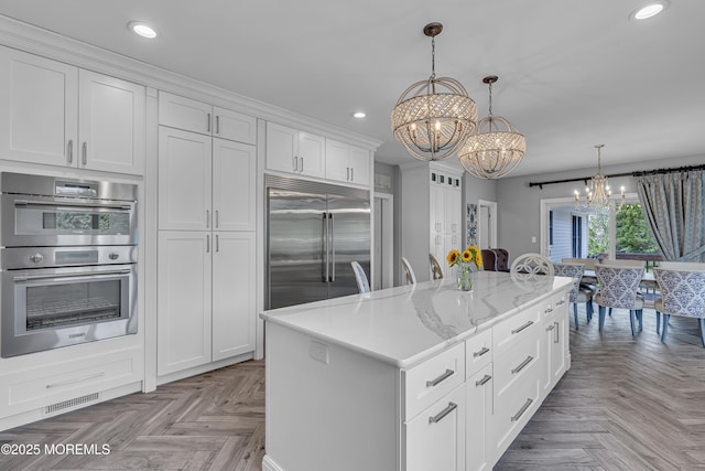 kitchen with appliances with stainless steel finishes, white cabinets, a center island, light parquet floors, and an inviting chandelier