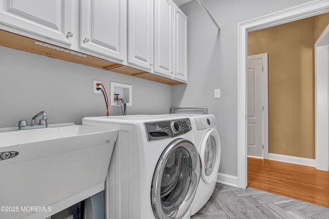 clothes washing area with sink, washing machine and clothes dryer, cabinets, and light parquet flooring