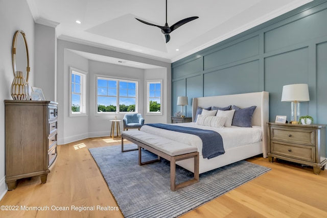 bedroom with ornamental molding, a tray ceiling, ceiling fan, and light hardwood / wood-style flooring