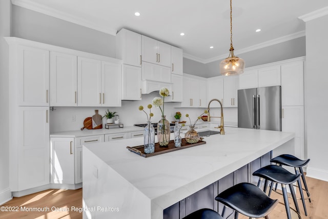 kitchen with crown molding, high end fridge, a kitchen island with sink, light hardwood / wood-style floors, and white cabinets