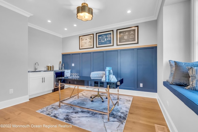 office space featuring crown molding, indoor wet bar, beverage cooler, and light hardwood / wood-style flooring