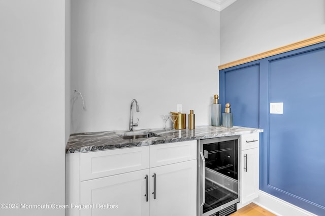 bar with sink, white cabinetry, ornamental molding, dark stone counters, and beverage cooler