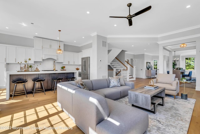 living room featuring crown molding, ceiling fan with notable chandelier, and light hardwood / wood-style floors