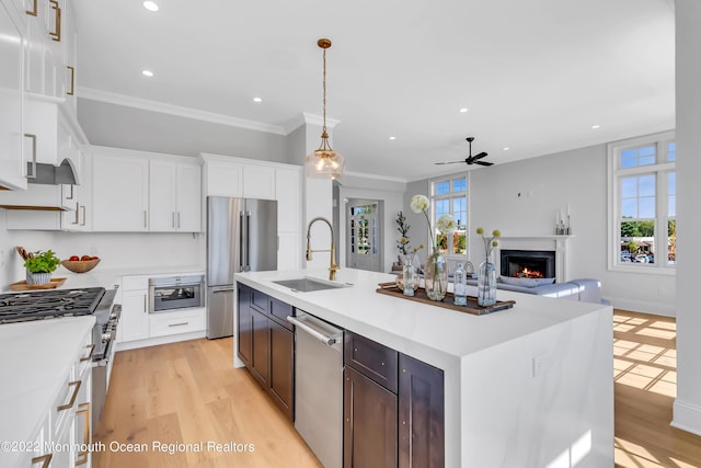 kitchen with decorative light fixtures, sink, white cabinets, high end appliances, and a center island with sink