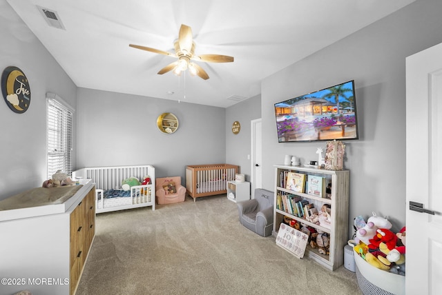 carpeted bedroom with a crib and ceiling fan