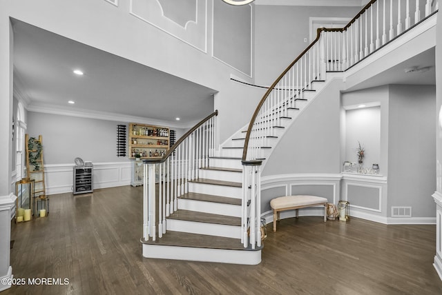 stairs with ornamental molding, bar area, hardwood / wood-style floors, and beverage cooler