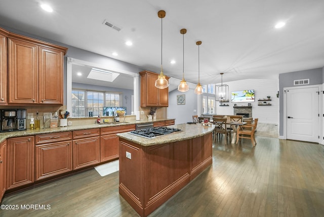 kitchen with stainless steel gas cooktop, light stone counters, dark hardwood / wood-style flooring, a kitchen island, and pendant lighting