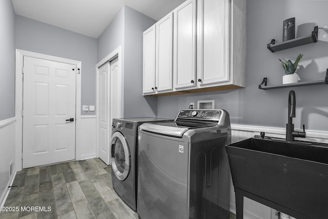 clothes washing area featuring separate washer and dryer, sink, light hardwood / wood-style flooring, and cabinets