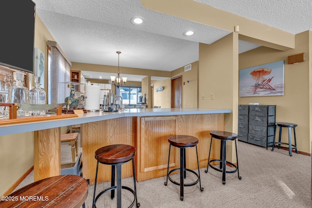 kitchen featuring a kitchen breakfast bar, kitchen peninsula, light carpet, a textured ceiling, and an inviting chandelier