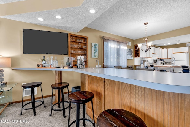 kitchen featuring a textured ceiling, hanging light fixtures, light carpet, a kitchen breakfast bar, and kitchen peninsula