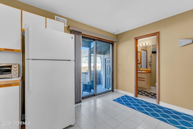 interior space featuring a textured ceiling, white cabinets, and white fridge