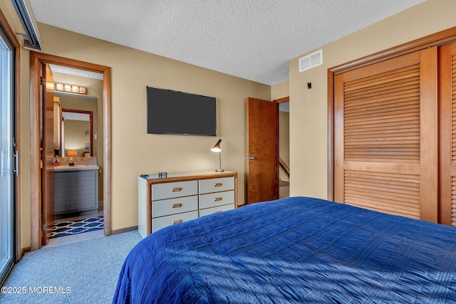 bedroom featuring ensuite bathroom, a textured ceiling, and light carpet