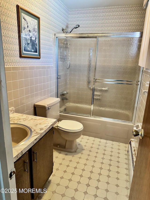 full bathroom featuring a baseboard heating unit, tile walls, toilet, vanity, and bath / shower combo with glass door