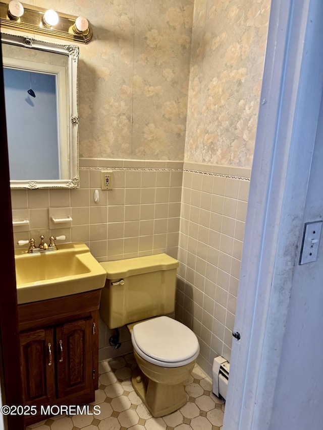 bathroom with toilet, vanity, a baseboard heating unit, and tile walls