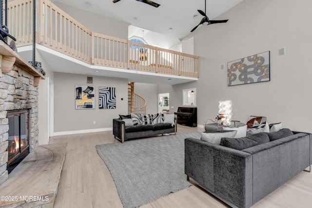 living room with a stone fireplace, a high ceiling, and ceiling fan