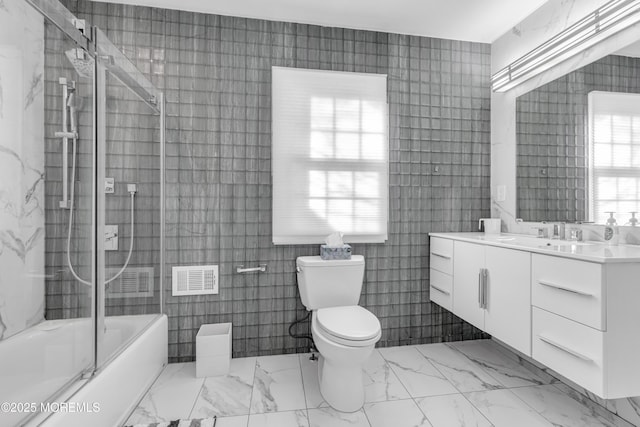 full bathroom featuring vanity, toilet, bath / shower combo with glass door, and tile walls