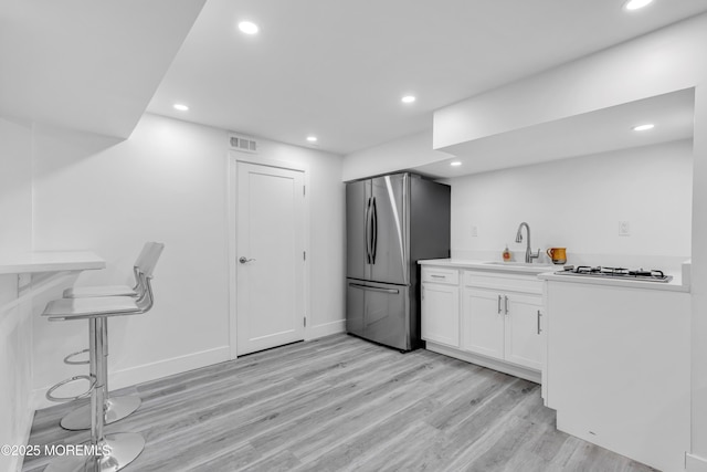 kitchen featuring sink, light wood-type flooring, white cabinetry, and stainless steel refrigerator