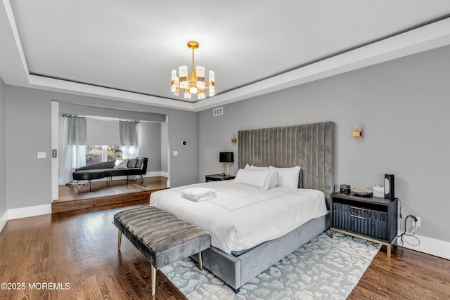 bedroom with wood-type flooring, a raised ceiling, and an inviting chandelier