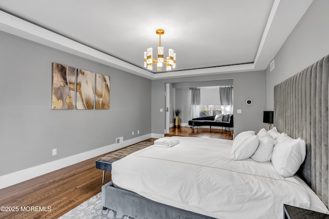 bedroom featuring an inviting chandelier, hardwood / wood-style floors, and a tray ceiling