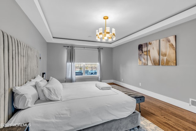 bedroom with hardwood / wood-style flooring, a tray ceiling, and a chandelier