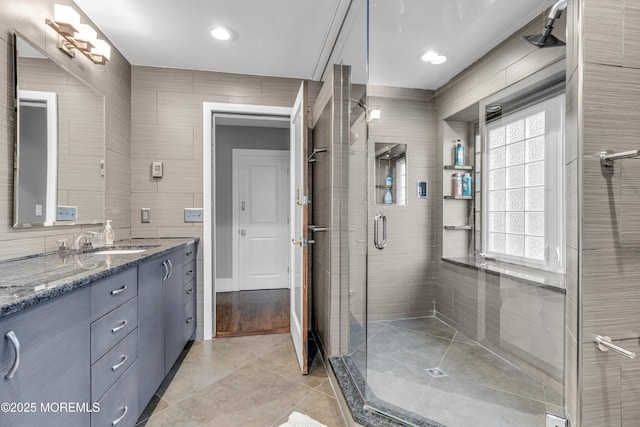 bathroom featuring a shower with door, tile patterned flooring, vanity, and tile walls