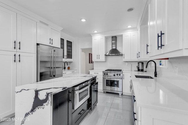 kitchen with sink, white cabinetry, light stone countertops, wall chimney range hood, and high end appliances