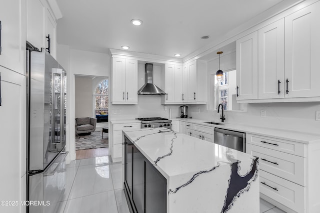 kitchen featuring appliances with stainless steel finishes, wall chimney range hood, sink, hanging light fixtures, and light stone counters