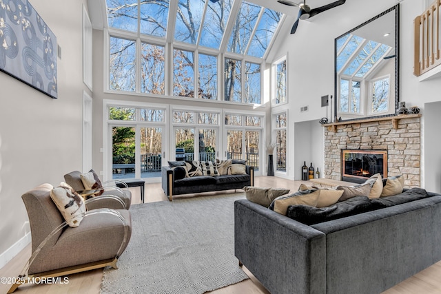 living room with ceiling fan, a high ceiling, a stone fireplace, and light hardwood / wood-style floors