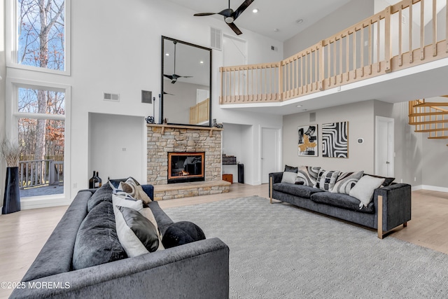 living room featuring ceiling fan, a high ceiling, hardwood / wood-style floors, and a stone fireplace