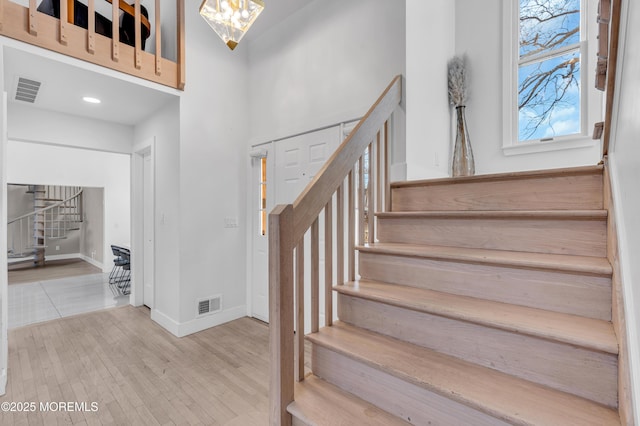 stairs with a towering ceiling, an inviting chandelier, and hardwood / wood-style floors