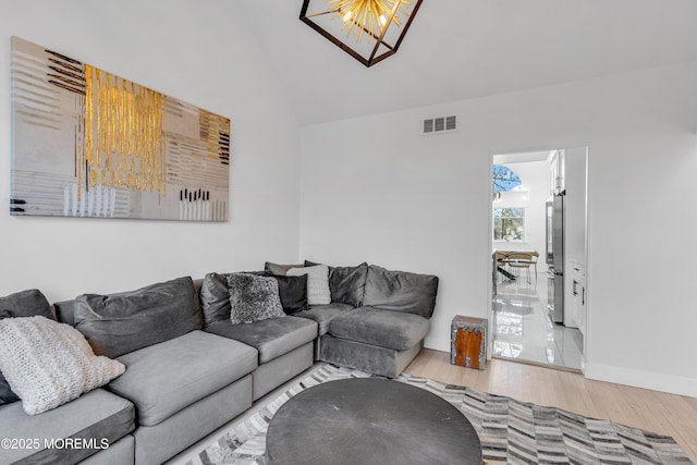 living room featuring an inviting chandelier, light hardwood / wood-style flooring, and vaulted ceiling