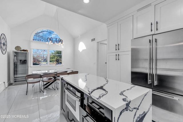 kitchen featuring light stone countertops, appliances with stainless steel finishes, white cabinetry, hanging light fixtures, and vaulted ceiling