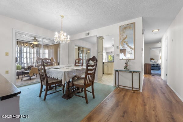 dining space with wood-type flooring, ceiling fan with notable chandelier, and a textured ceiling