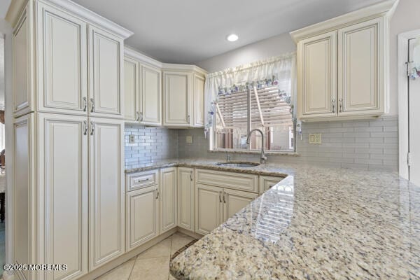 kitchen featuring sink, light stone counters, light tile patterned floors, cream cabinets, and backsplash