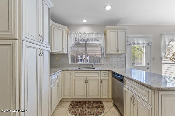 kitchen with dishwasher, sink, kitchen peninsula, light stone countertops, and cream cabinetry