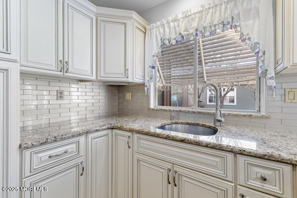 kitchen featuring tasteful backsplash, light stone countertops, sink, and white cabinets