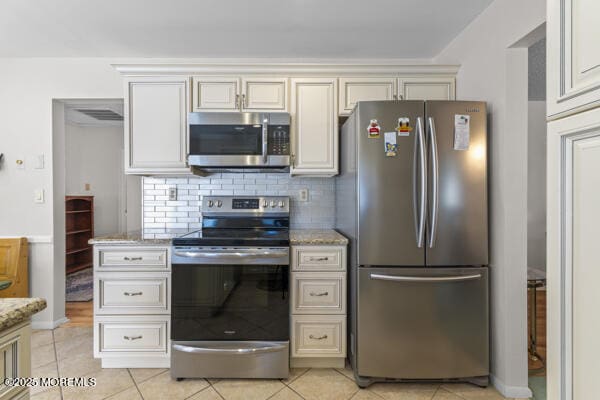 kitchen with light tile patterned flooring, stainless steel appliances, light stone countertops, and decorative backsplash