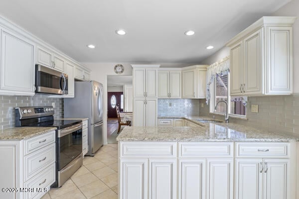 kitchen with appliances with stainless steel finishes, sink, light tile patterned floors, light stone counters, and kitchen peninsula