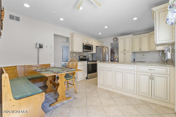 kitchen with appliances with stainless steel finishes, sink, light tile patterned floors, light stone counters, and cream cabinets