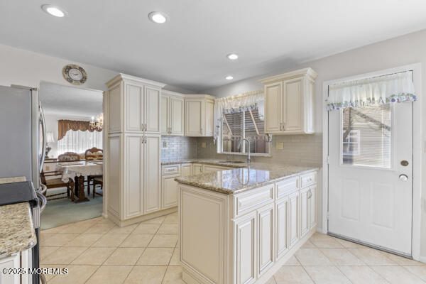 kitchen featuring sink, light tile patterned floors, light stone counters, tasteful backsplash, and cream cabinetry