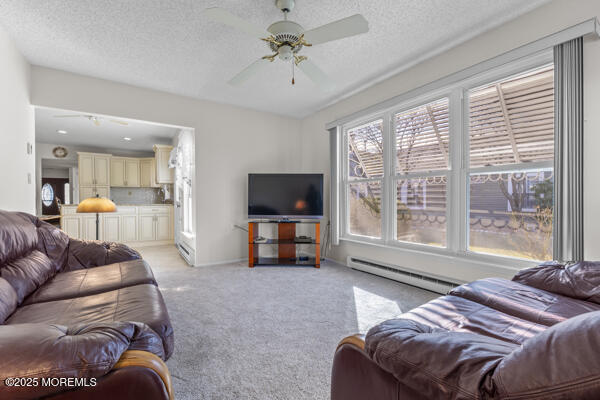 living room with ceiling fan, a baseboard heating unit, light carpet, and a textured ceiling